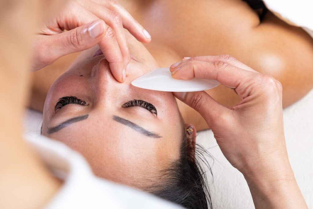 gros plan sur une main passant un gua sha sur le visage d'une cliente pour illustrer les bienfaits des massages en entreprise